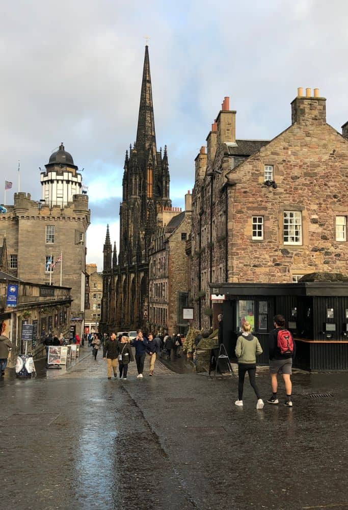 A view of the Royal Mile in Edinburgh from Edinburgh Castle. The streets are shiny from recent rain and old architectural buildings stand tall in the background.